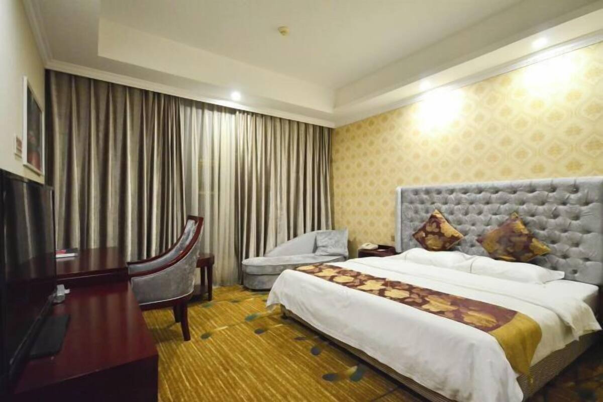 A hotel room with a bed, a desk, a chair, and a large window with curtains.