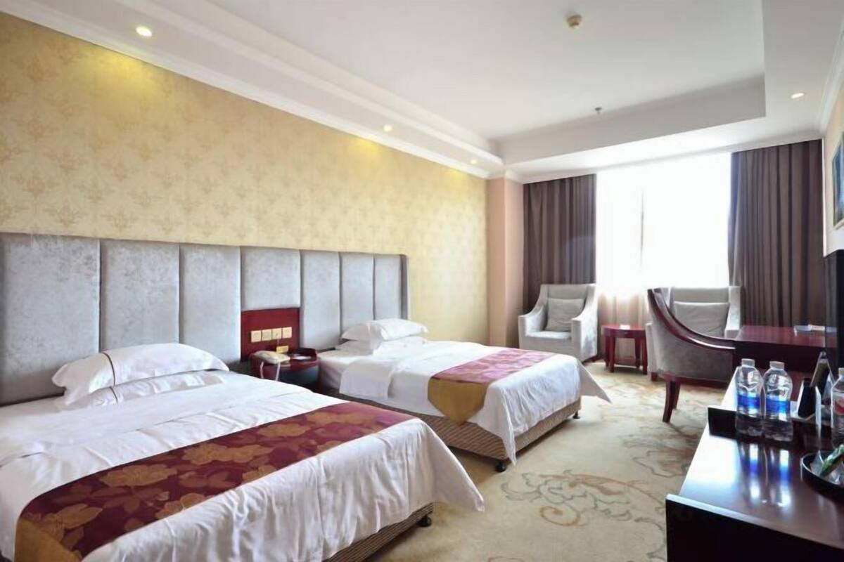 A hotel room with two beds, a desk, a chair, and a TV.