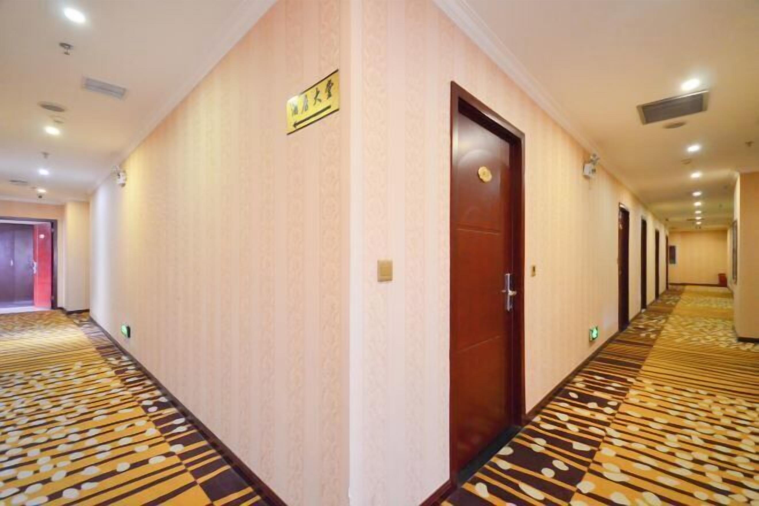 Un couloir d’hôtel avec un tapis à motifs, une porte en bois et un panneau sur le mur.