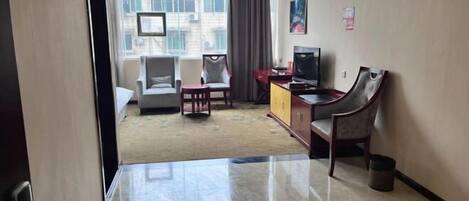 Quarto de hotel com uma janela grande, televisão, escrivaninha e uma cadeira.