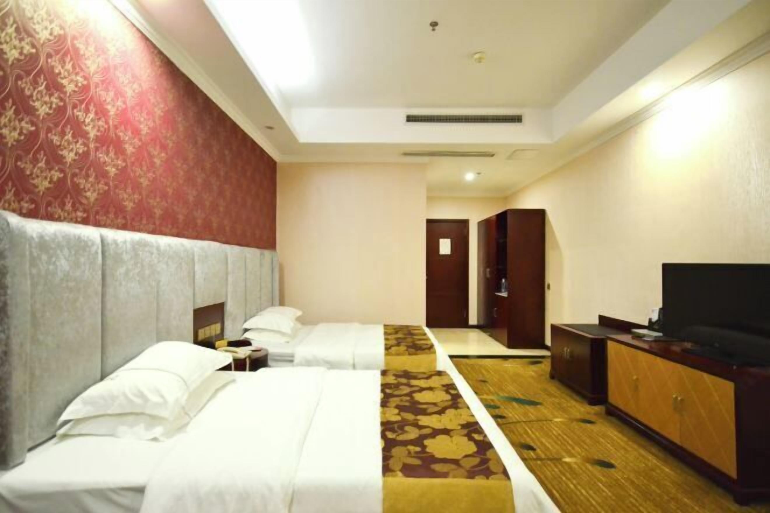 A hotel room with two beds, a television, a wardrobe, and a carpeted floor.
