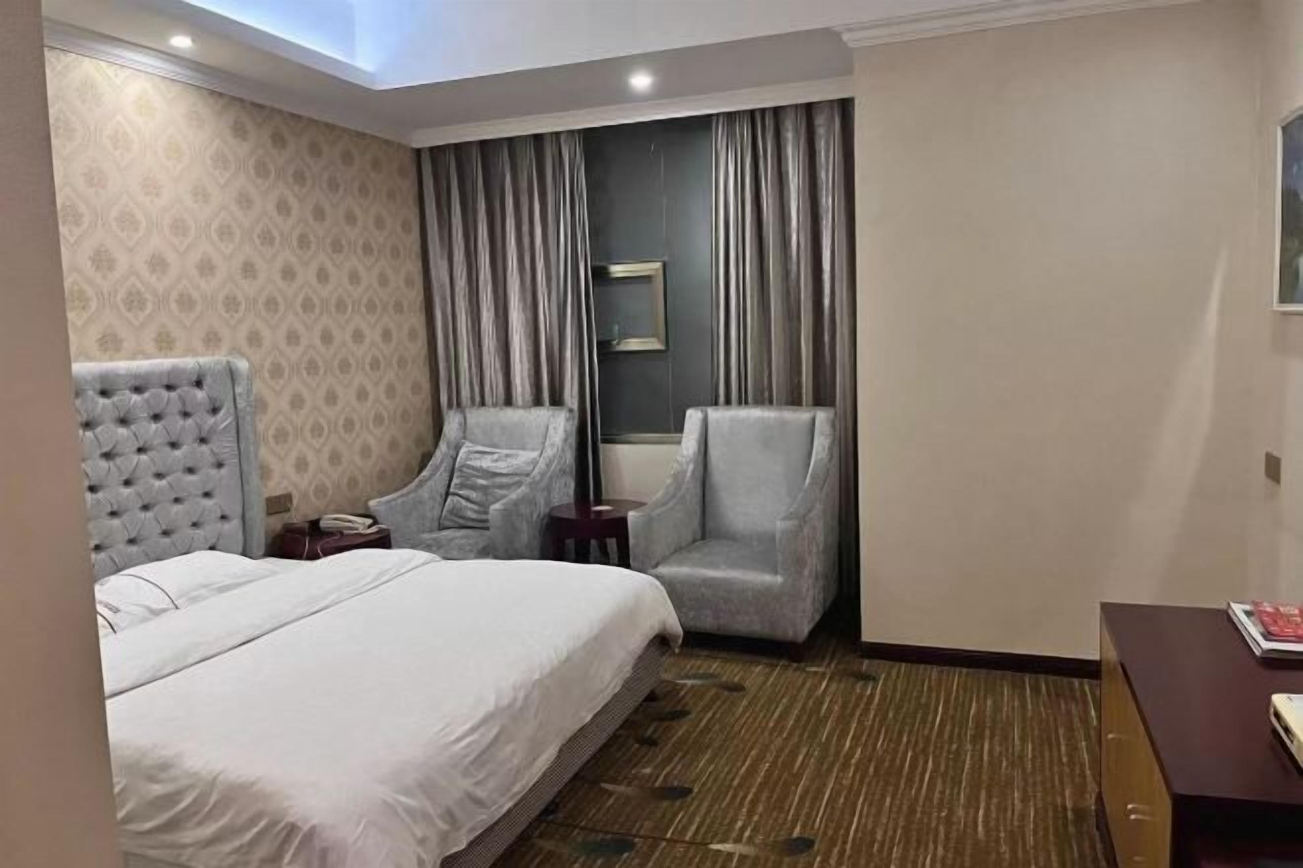 Ein Hotelzimmer mit einem großen Bett, zwei Sesseln, einem kleinen Tisch und einem Spiegel an der Wand.