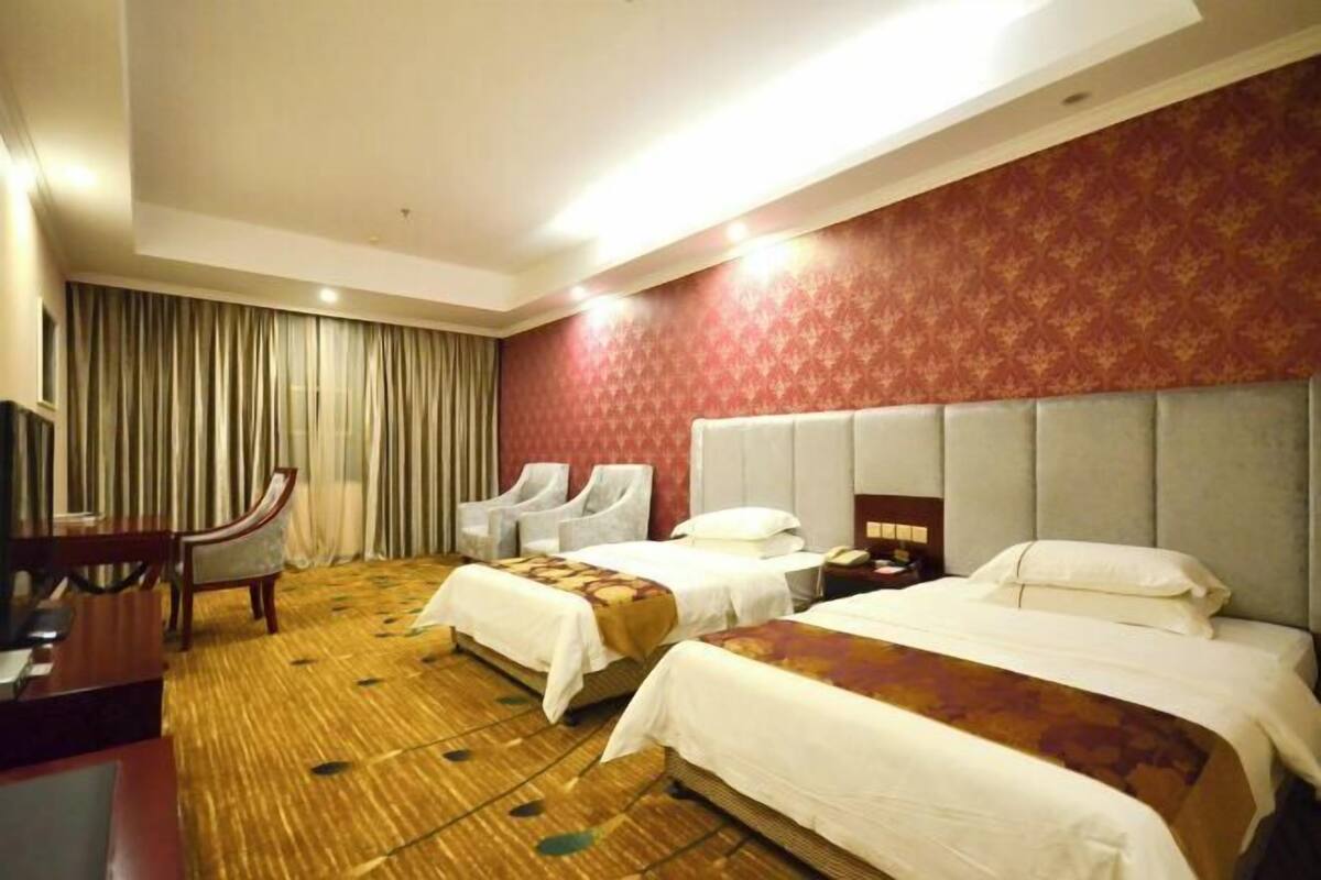 A hotel room with two beds, a desk, a chair, and a television.