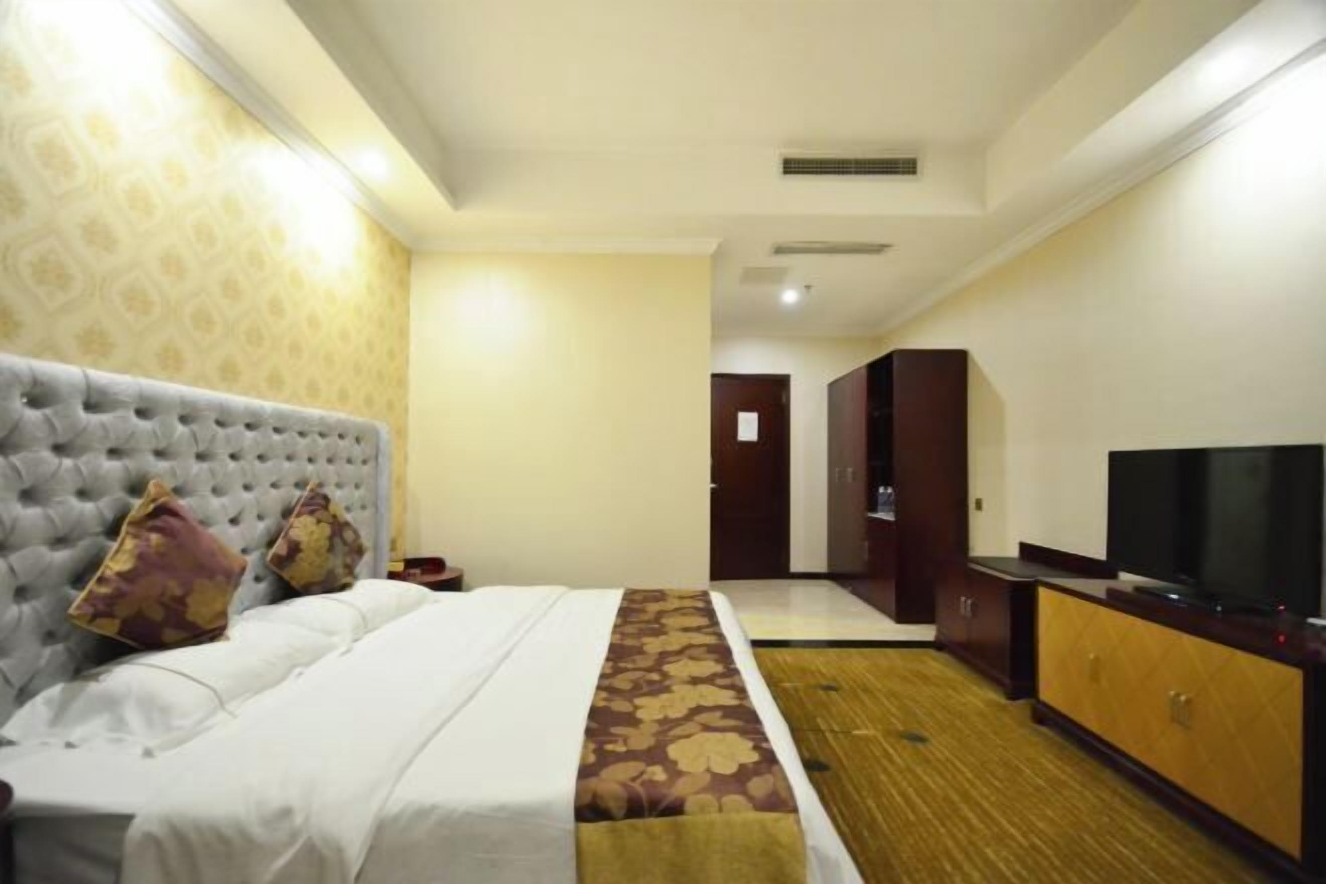 A hotel room with a bed, a television, a wardrobe, and a door leading to another room.