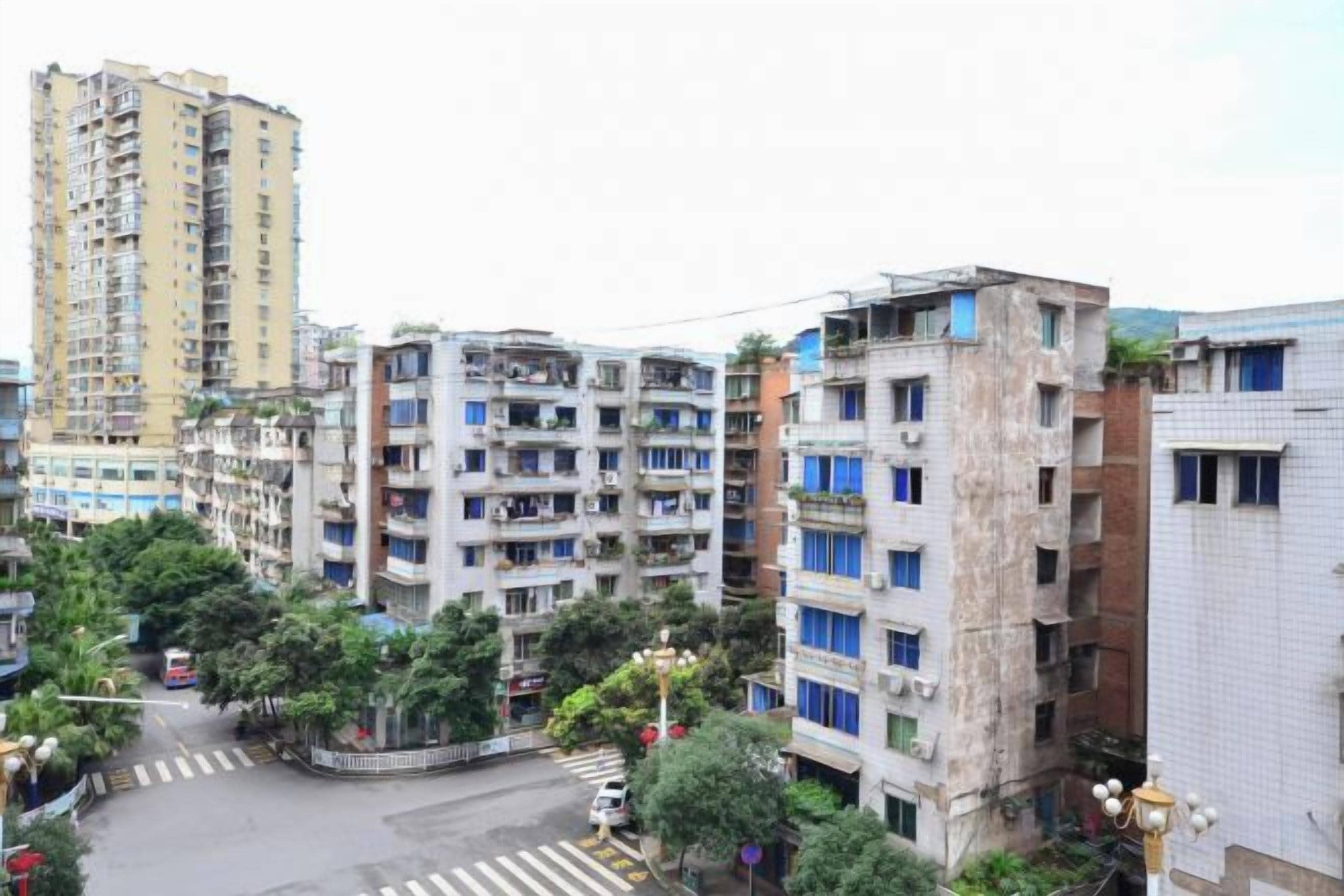 A multi-story residential building with balconies, a pedestrian crossing, and a street with a bus.