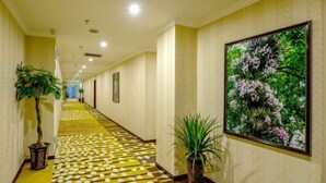 A hotel hallway with patterned carpet, potted plants, and a large floral painting on the wall. - Siyuan Hotel (Chishui)