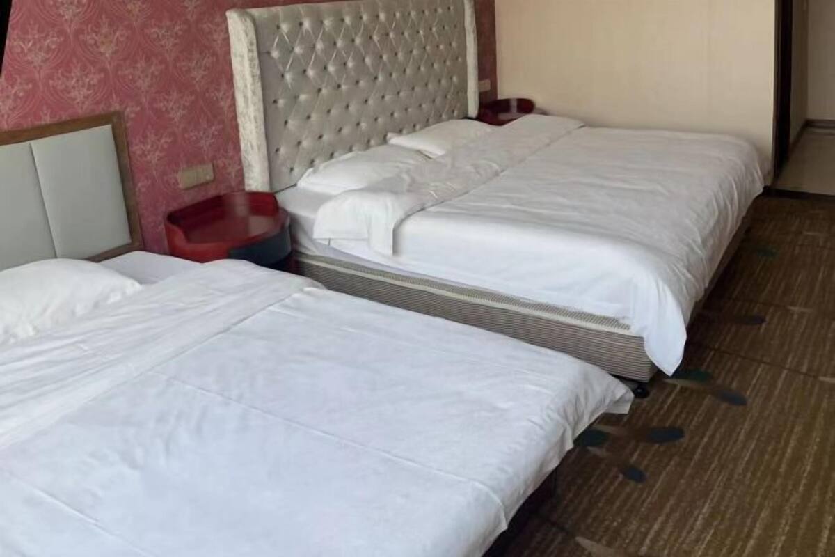 A hotel room with two beds, a red plastic chair, and a patterned wall.