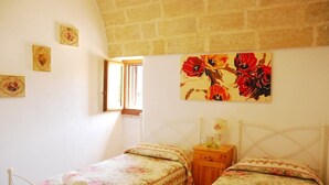 Une chambre avec deux lits simples, une table de chevet en bois, une fenêtre et un tableau représentant des motifs floraux accroché au mur.