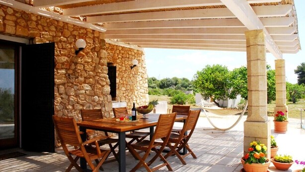 Un espace extérieur abrité, aménagé pour les repas, avec des murs en pierre, des chaises en bois et des plantes en pot.