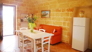 Une cuisine avec une table blanche, des chaises, un canapé rouge, un réfrigérateur blanc et un vase avec des fleurs accroché au mur.