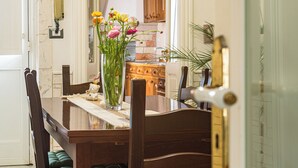 A wooden dining table with a vase of flowers, chairs, and a kitchen in the background. - Exclusive Private Villa with Pool & Jacuzzi Surrounded by Citrus Trees – Salento (Taviano)