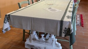 A dining room with a long table, chairs, a white cabinet with glass doors, and a patterned tablecloth.