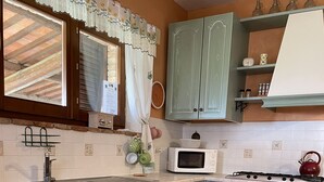 A kitchen with light green cabinets, a white microwave, a red kettle, and a red patterned rug.