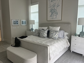 A bedroom with a large bed, bedside tables, a bench, and a wall-mounted artwork.