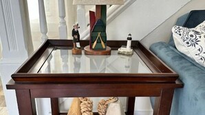 Una mesita de madera con tapa de vidrio, una lámpara, una figurita pequeña y dos objetos decorativos con cuerdas y números.