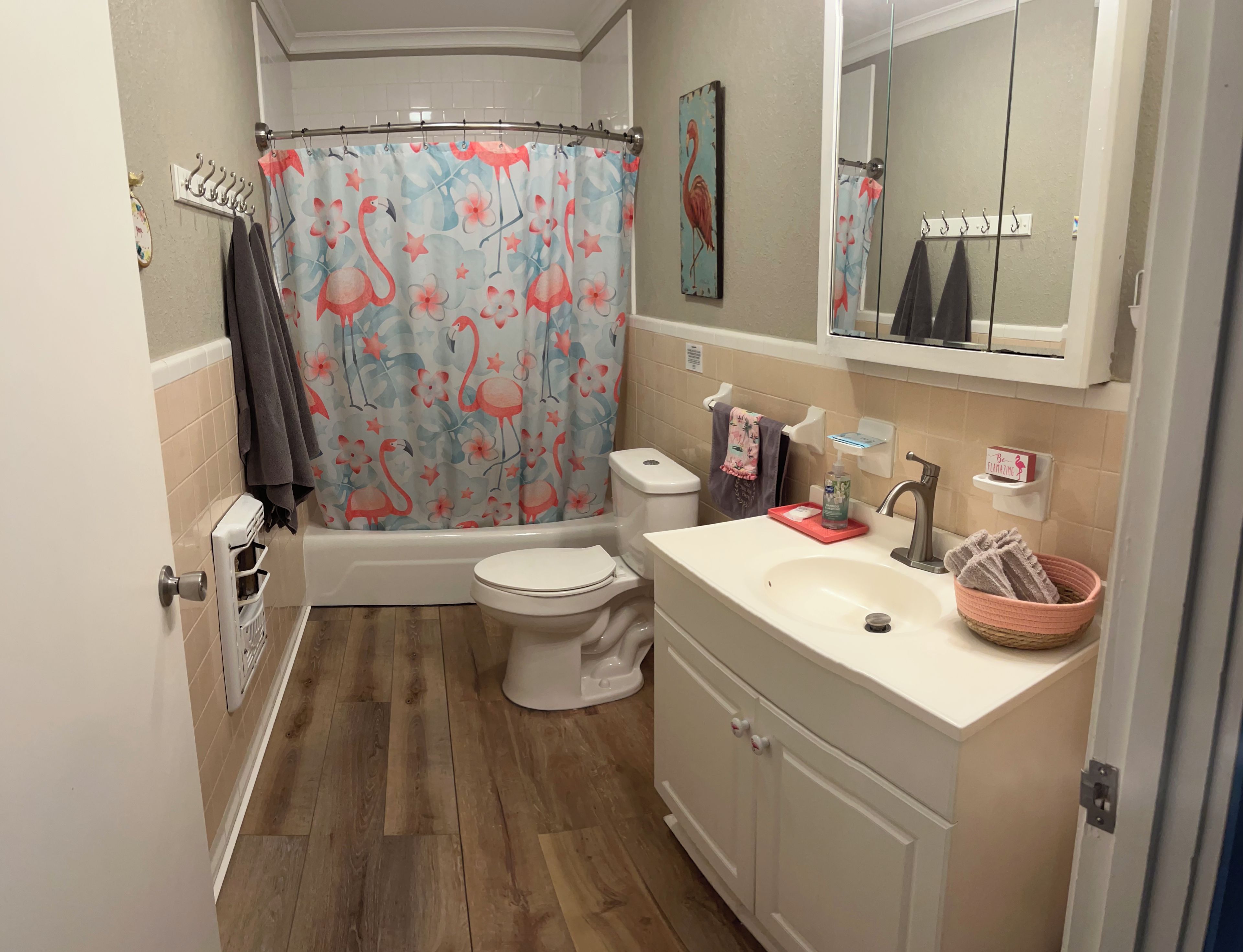 Une salle de bain équipée d’un rideau de douche orné de flamants roses, de toilettes, d’un lavabo avec un distributeur de savon et d’un porte-serviettes.
