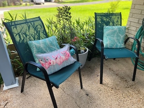 Two outdoor chairs with teal cushions and a floral pattern, a potted plant, and a concrete patio.