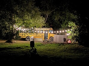 Ein gelber Bus, der nachts in bewaldeter Landschaft steht, umgeben von Lichterketten.
