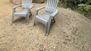 Two Adirondack chairs, a wooden deck, and a school bus in a wooded area.
