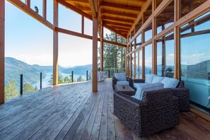 Terraza de madera con mobiliario de mimbre, con vistas a un lago y montañas.