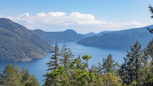 A panoramic view of a lake surrounded by forested mountains. - The Summit Room suite  – Breathtaking Fjord View at the Summit House. (Malahat)