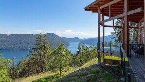 A wooden cabin with a balcony overlooking a lake and mountains. - The Summit Room suite  – Breathtaking Fjord View at the Summit House. (Malahat)
