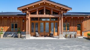 A wooden lodge with a stone foundation, large glass doors, and a covered porch area. - The Summit Room suite  – Breathtaking Fjord View at the Summit House. (Malahat)