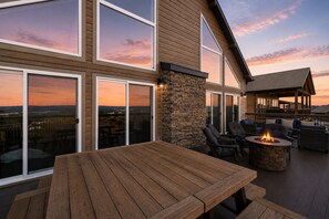 Eine Terrasse mit Holztisch und -stühlen, einem Steinkamin und großen Schiebeglastüren mit Blick auf die Landschaft.