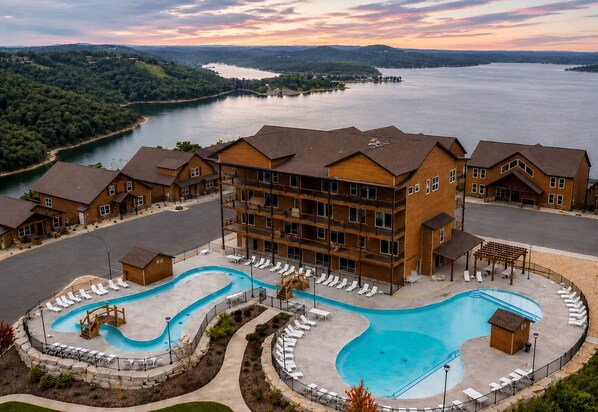 Un resort con una piscina grande, varias habitaciones y vista a un lago.