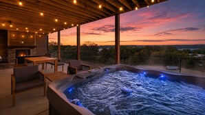 A hot tub with a view of the sunset, wooden furniture, and a stone fireplace. - Hot Tub, Lake & Mtn Views, King Beds, Bunk Room (Kimberling City)