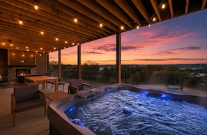 Un jacuzzi con vista al atardecer, mobiliario de madera y una chimenea de piedra.