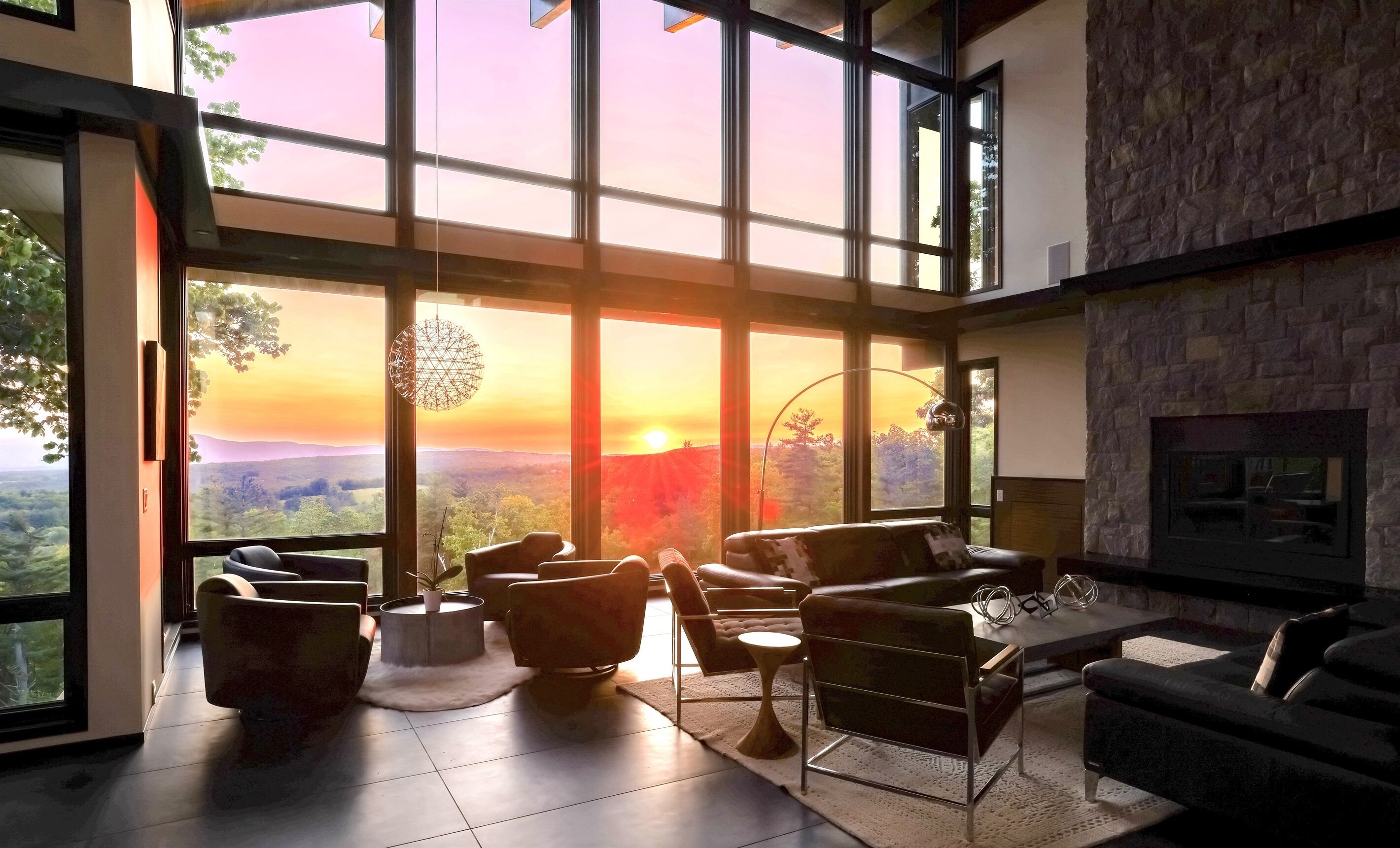 Ein geräumiges Wohnzimmer mit großen Fenstern und einem herrlichen Blick auf einen Sonnenuntergang über einem Tal.