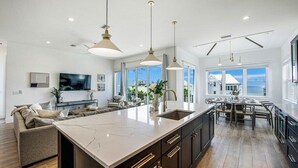 A modern kitchen with a large island, dark cabinetry, and pendant lighting. - Mariner's Crossing – Luxury Escape w/ Rooftop Deck, Pool, Spa & Game Room (Bradenton Beach)