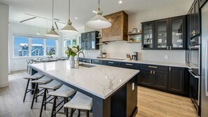 A modern kitchen with a large island, dark cabinetry, and pendant lighting. - Mariner's Crossing – Luxury Escape w/ Rooftop Deck, Pool, Spa & Game Room (Bradenton Beach)