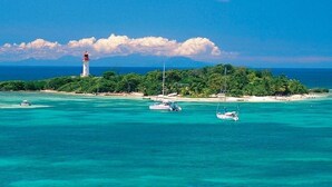 Una isla tropical con un faro, aguas turquesas cristalinas y embarcaciones.