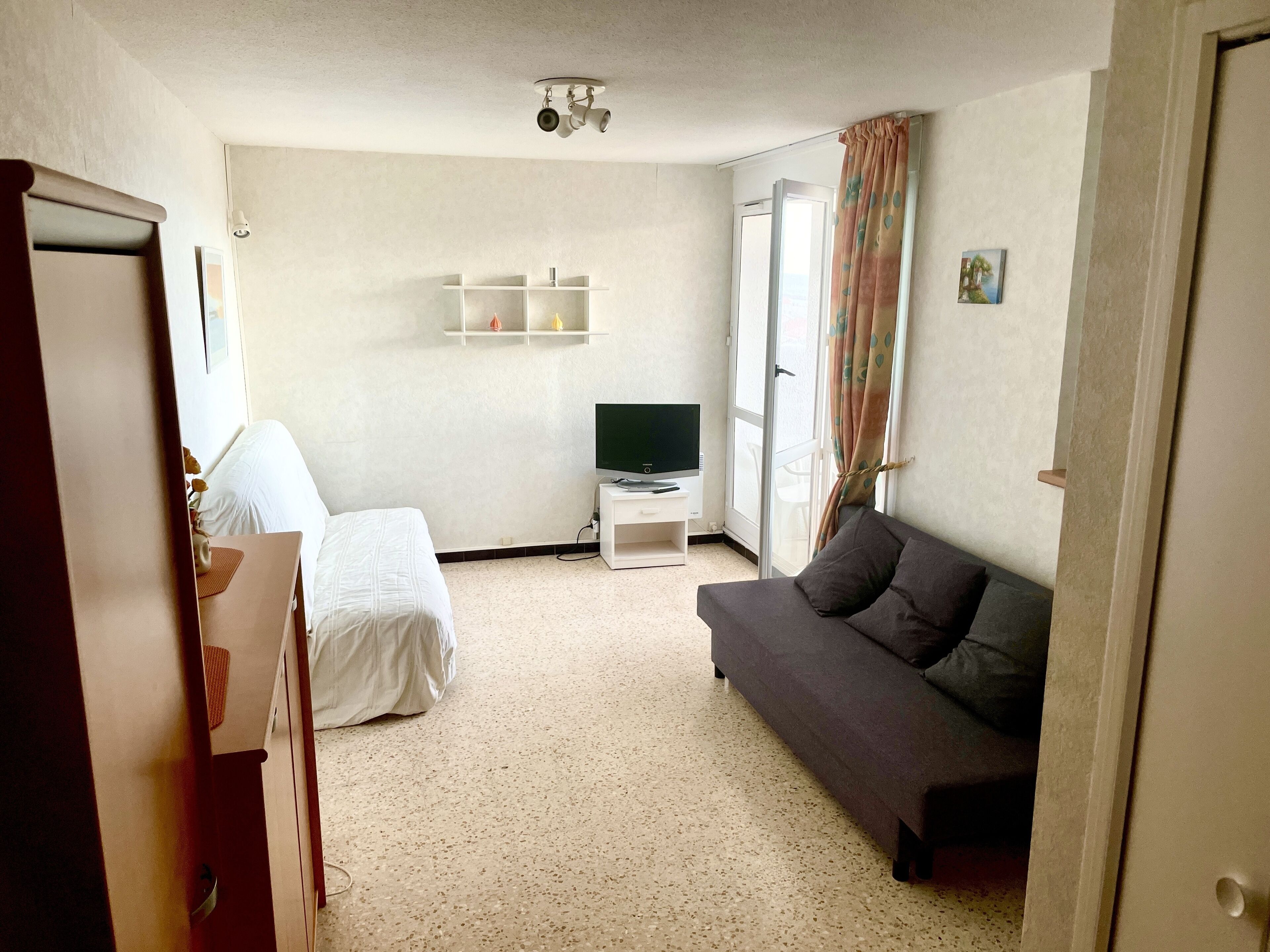 A hotel room with a bed, a sofa, a TV on a stand, and a window with curtains.