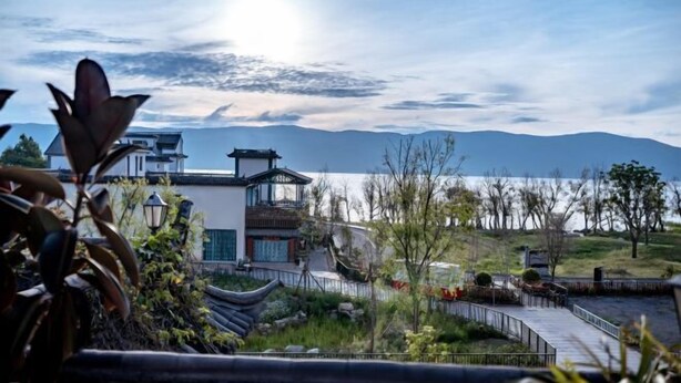 A traditional-style building with a modern extension, a bridge, and a view of mountains and a body of water. - Jiayu Seascape Inn (Dali City)