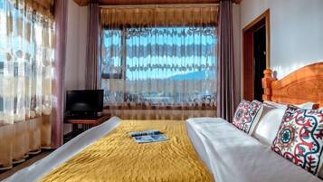 Una habitación de hotel con una cama, televisión y ventana con cortinas.