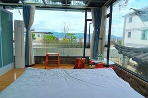 A room with a bed, a small stool, and a window with a view of buildings and mountains. - Jiayu Seascape Inn (Dali City)