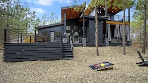 Una cabaña moderna de dos pisos con terraza de madera y zona de estar exterior cubierta.