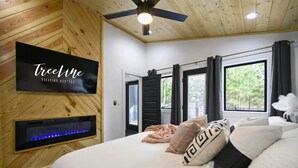 Un dormitorio con cama, televisión instalada, chimenea y ventana con cortinas.