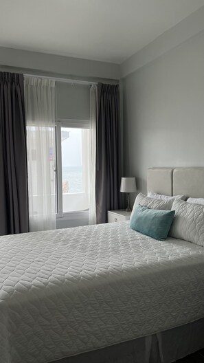 Une chambre d’hôtel avec un grand lit, une table de chevet avec une lampe et une vue sur la mer par la fenêtre.