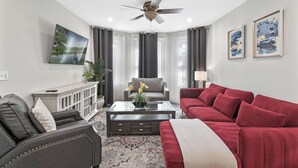 Ein modernes Wohnzimmer mit Deckenventilator, einem grauen Sofa, einem roten Sofa, einem Couchtisch und einem Gemälde an der Wand.