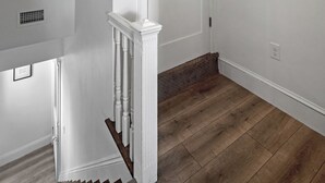 Ein helles Interieur mit einer Holztreppe, einer weißen Tür mit der Nummer 3 und einem Lüftungsgitter an der Wand.