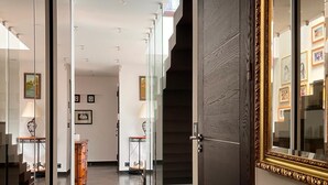 Um corredor moderno com portas de vidro, uma porta de madeira escura e uma escadaria.