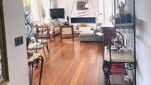 Uma sala de estar ampla com piso de madeira, um sofá, uma televisão e uma mesa de jantar.