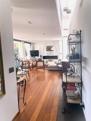 A spacious living area with a wooden floor, a sofa, a television, and a dining table.