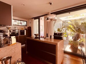 A modern kitchen with a central island, built-in appliances, and a large window overlooking a garden. - Villa Palma – California Elegance, 12-meter Pool, Rooftop, and Ocean View (Fréjus)