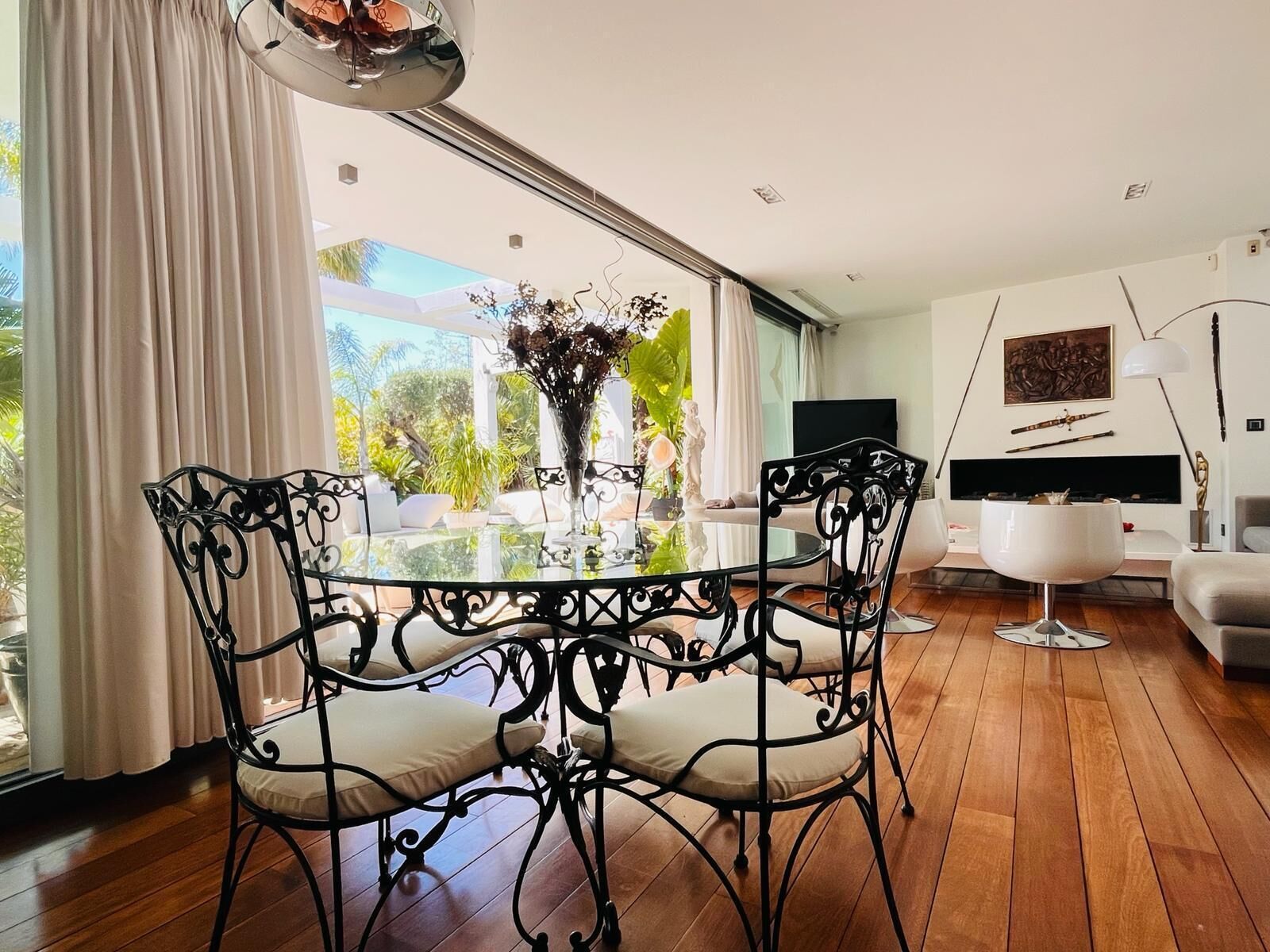 A modern dining area with a glass table, black metal chairs, and a vase of flowers.