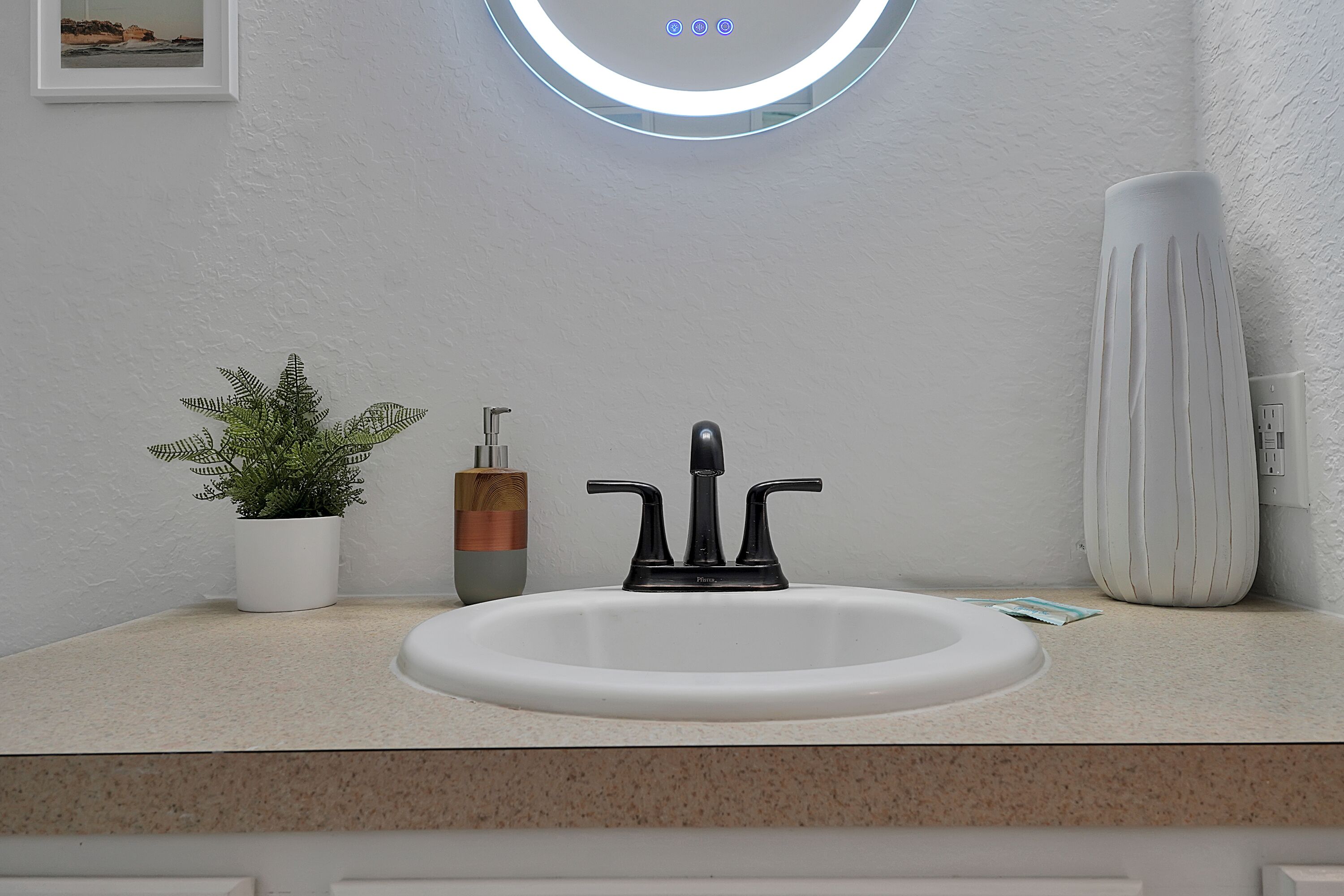 A bathroom with a white sink, a modern faucet, a potted plant, and a decorative vase.